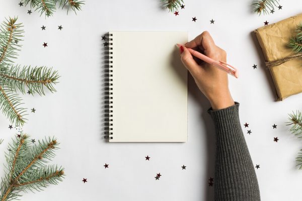Goals plans dreams make to do list for new year christmas concept writing in notebook. Woman hand holding pen on notebook with fir branches gift on white background. New year winter holiday xmas